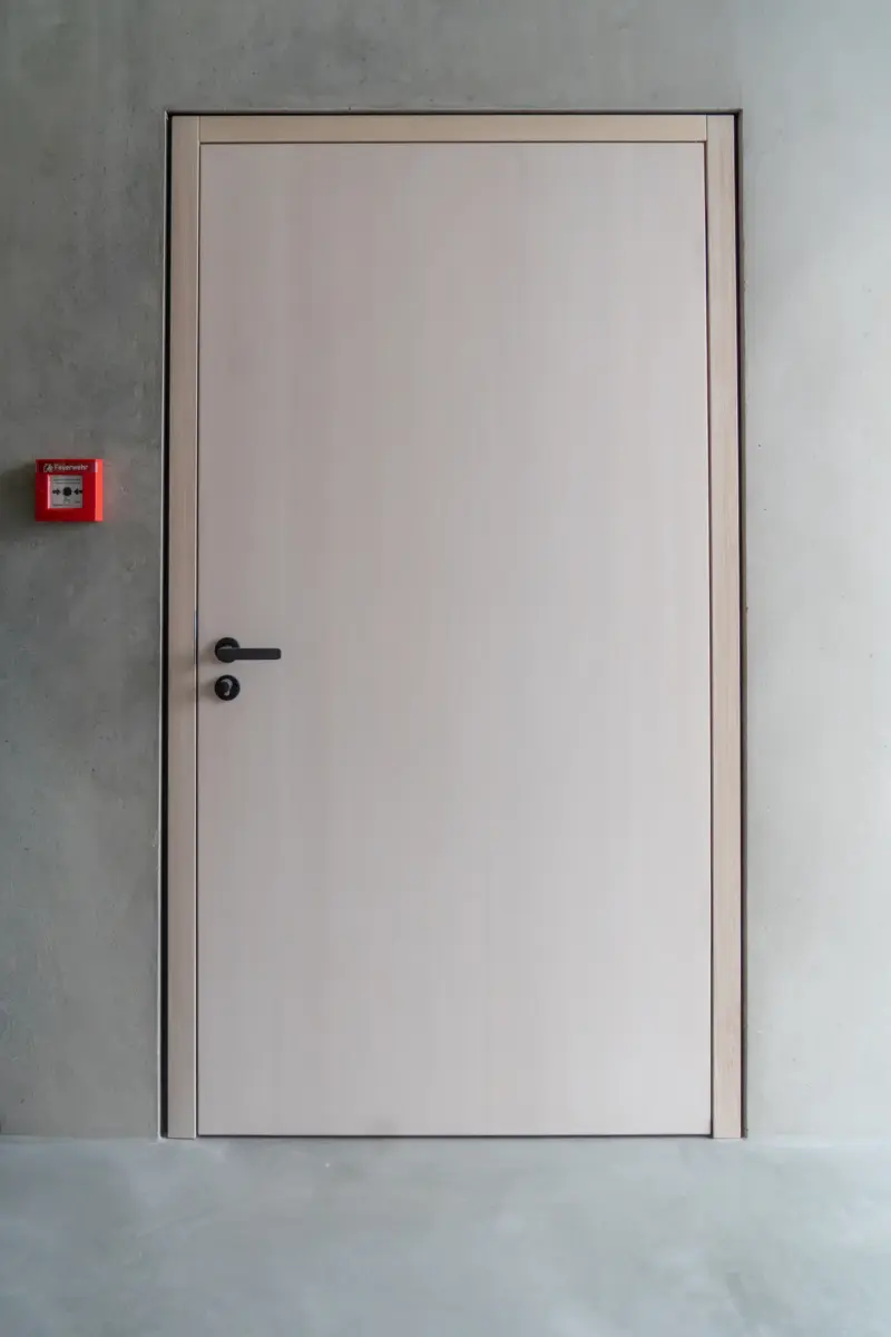 Geschlossene helle Holztür mit dunklem Griff in einer grauen Wand.